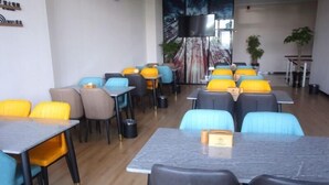 A modern dining area with multiple tables and chairs, a large screen on the wall, and a view of the outdoors. - Greentree Inn Fuyang Exhibition Center (Fuyang)