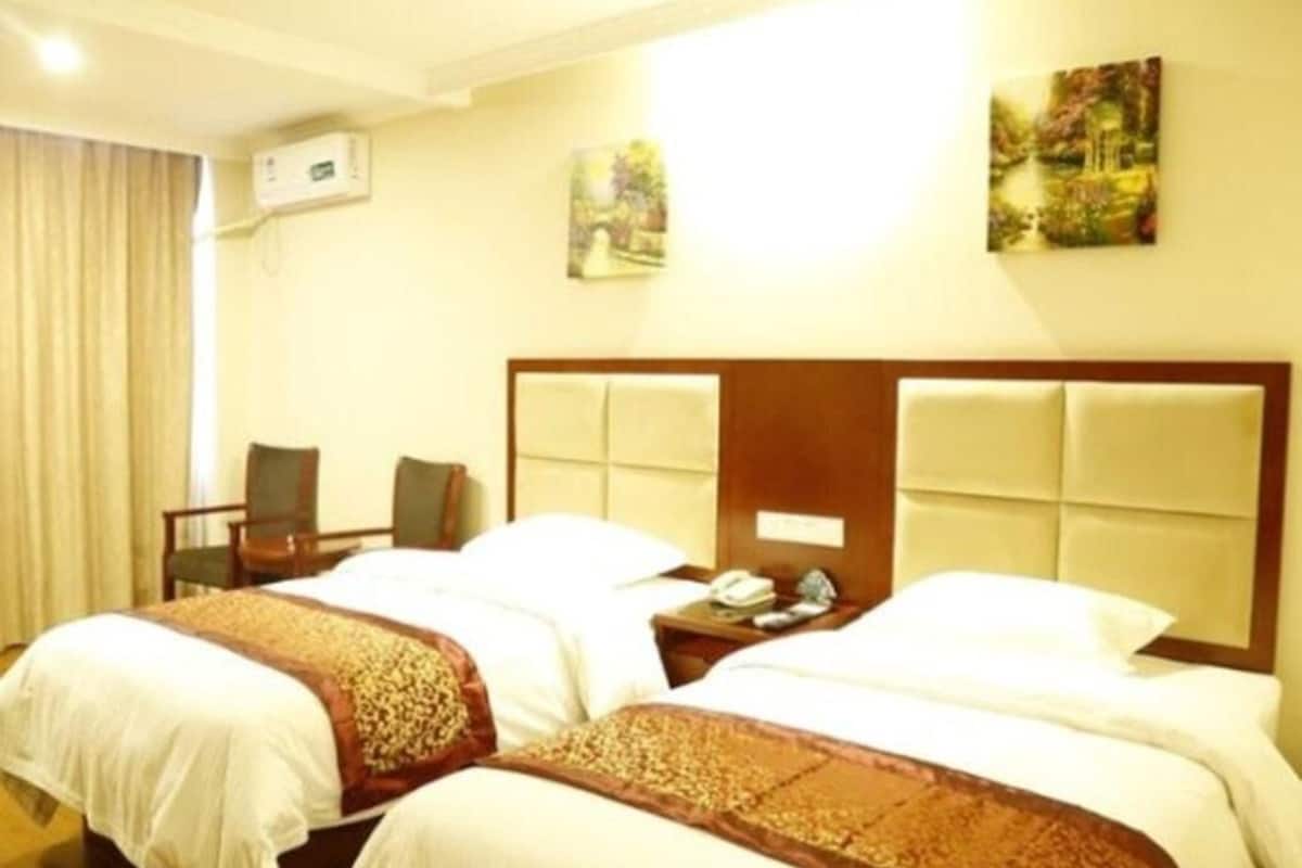 A hotel room with two beds, a desk, a chair, and a wall-mounted air conditioner.
