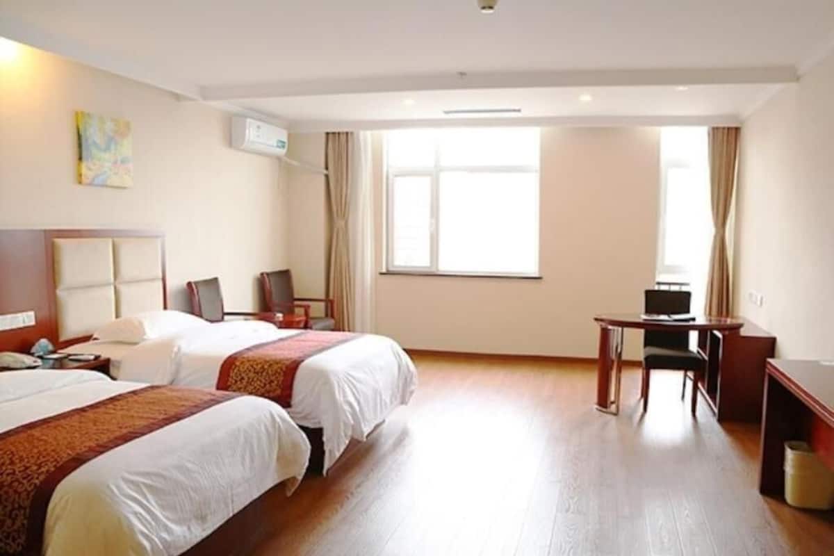 A hotel room with two beds, a desk, a chair, a TV, and a large window.