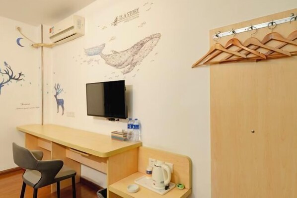 A room with a desk, chair, mounted TV, and a coat rack.