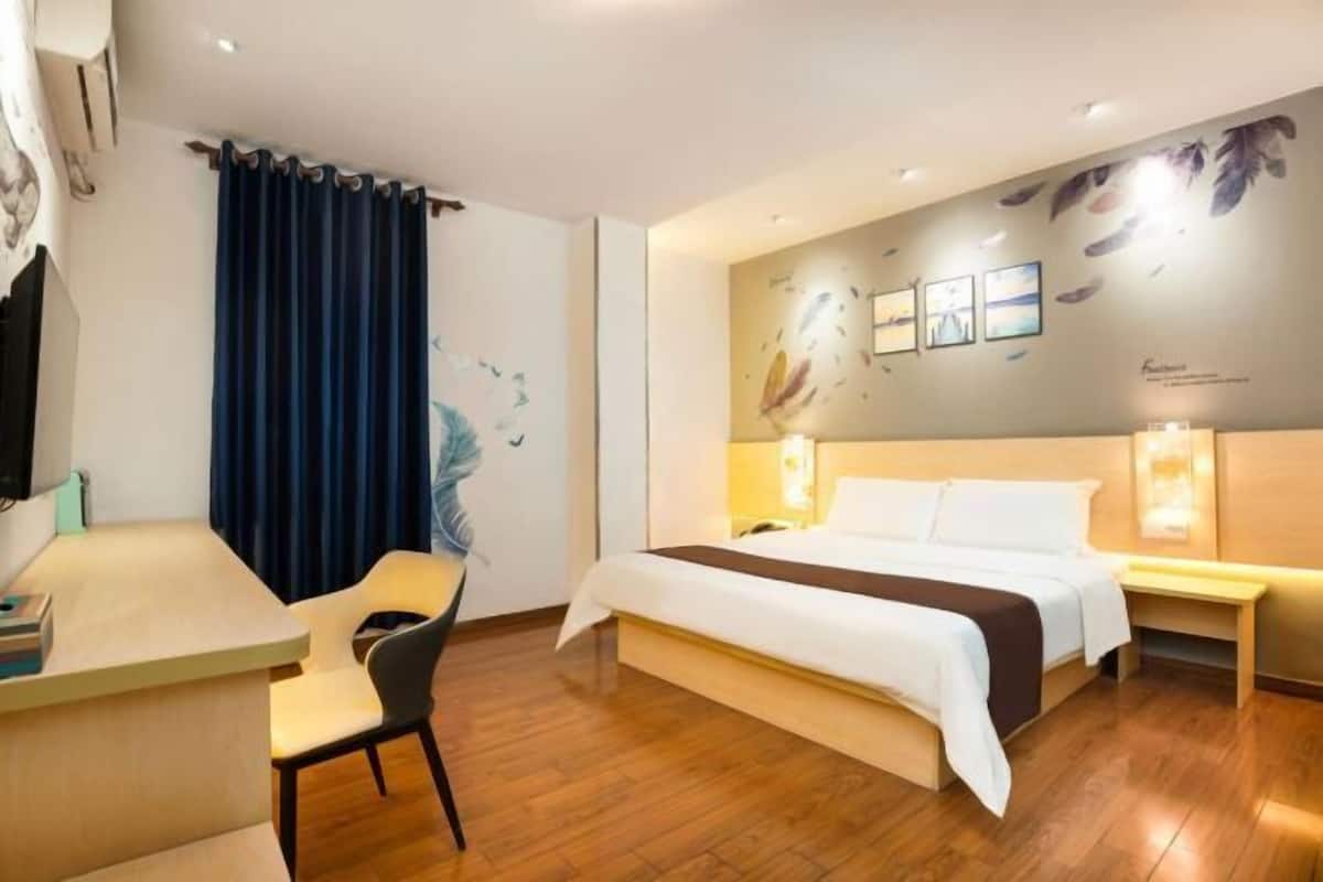 A hotel room with a bed, a desk, a chair, and a wall with feather artwork.