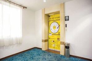 Une chambre d’hôtel avec un tapis à motifs bleus, une porte avec une pancarte jaune et une poubelle.