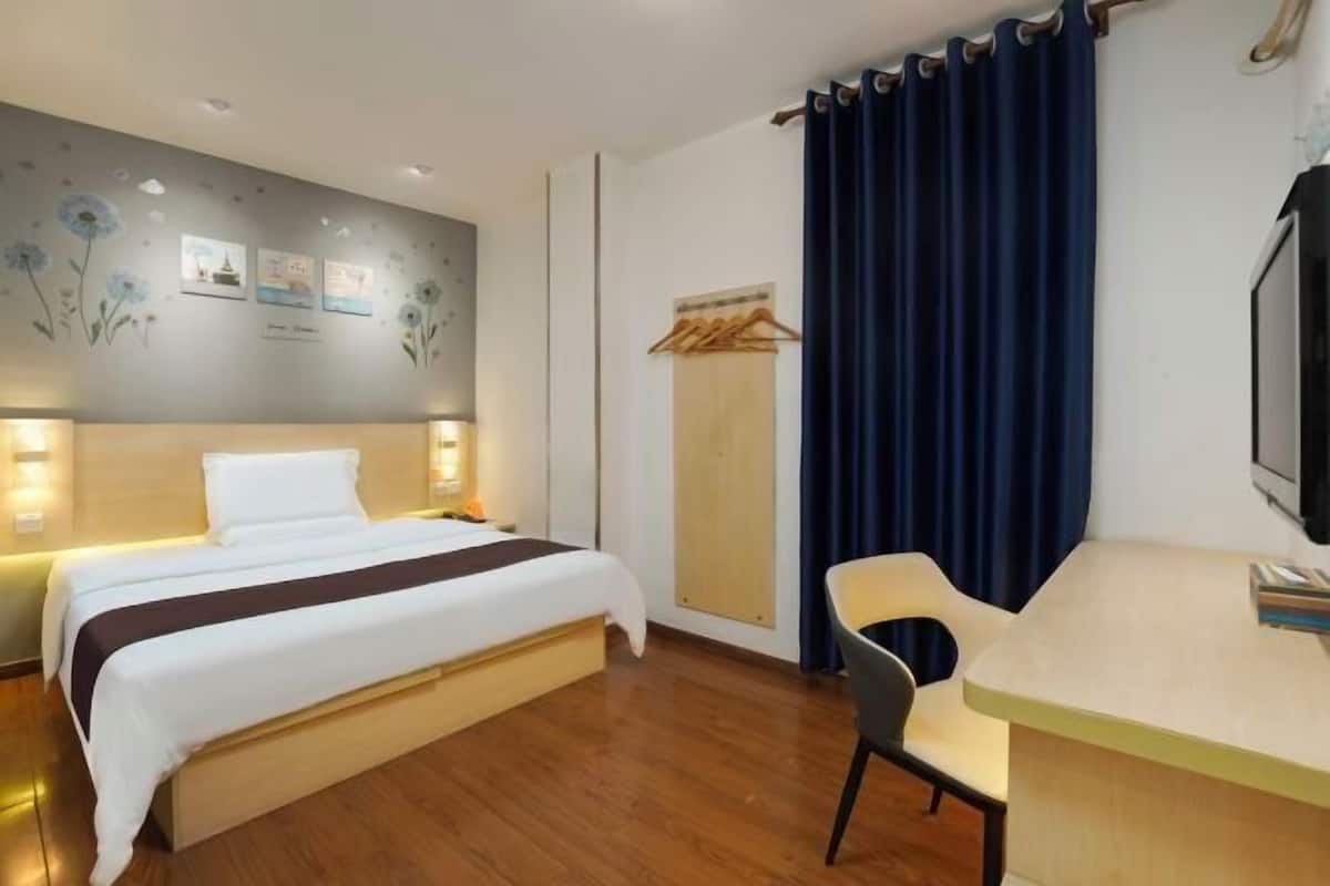 A hotel room with a bed, bedside table, chair, and a desk. There are wall decorations and a curtain.