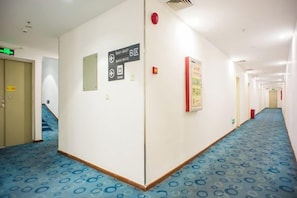 A hotel corridor with a blue patterned carpet, directional signs, and a fire alarm. - 7 Days Inn Jiangmen Qimingli Square Sanshisanxu Street Branch (Jiangmen)