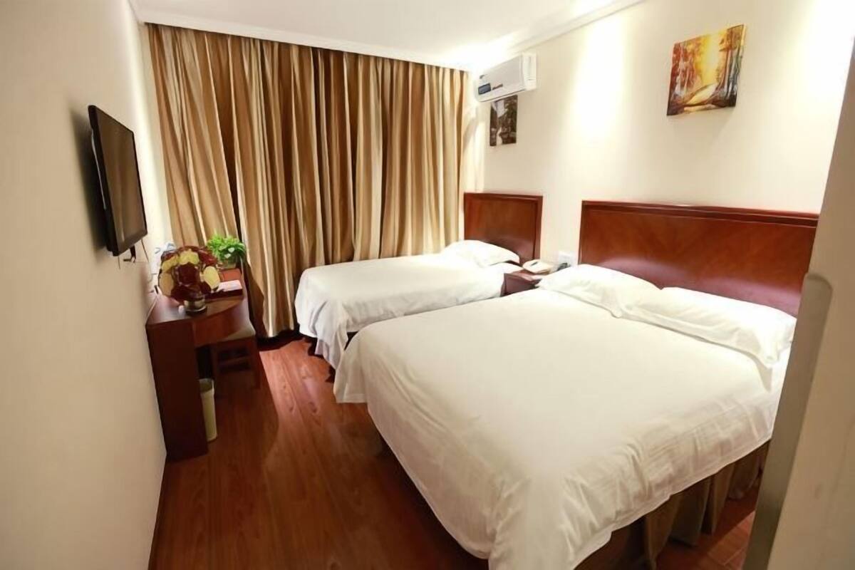 A hotel room with two beds, a desk with a lamp, a TV, and a window with curtains.
