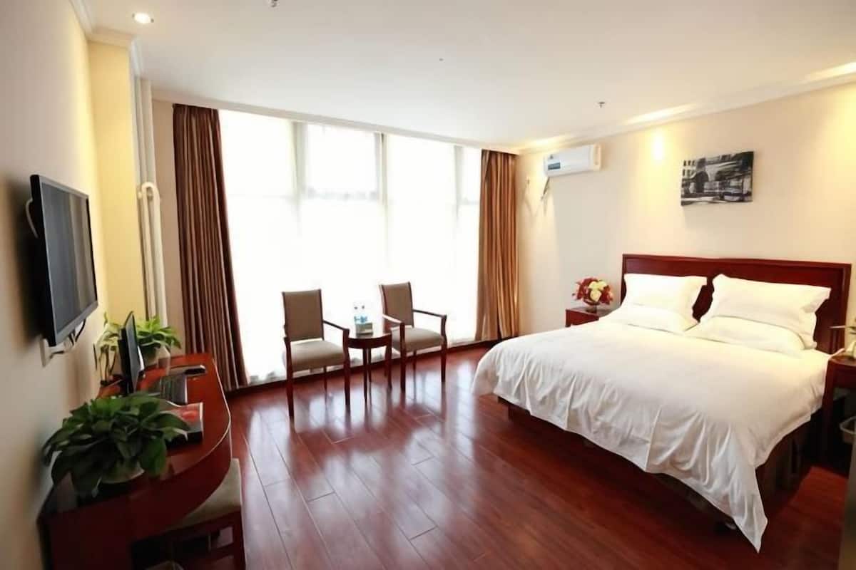 A hotel room with a bed, a desk with a chair, a TV, and a window with curtains.