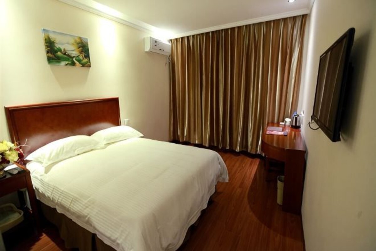 Ein Hotelzimmer mit Bett, Schreibtisch, Stuhl, Fernseher und einem Fenster mit Vorhängen.