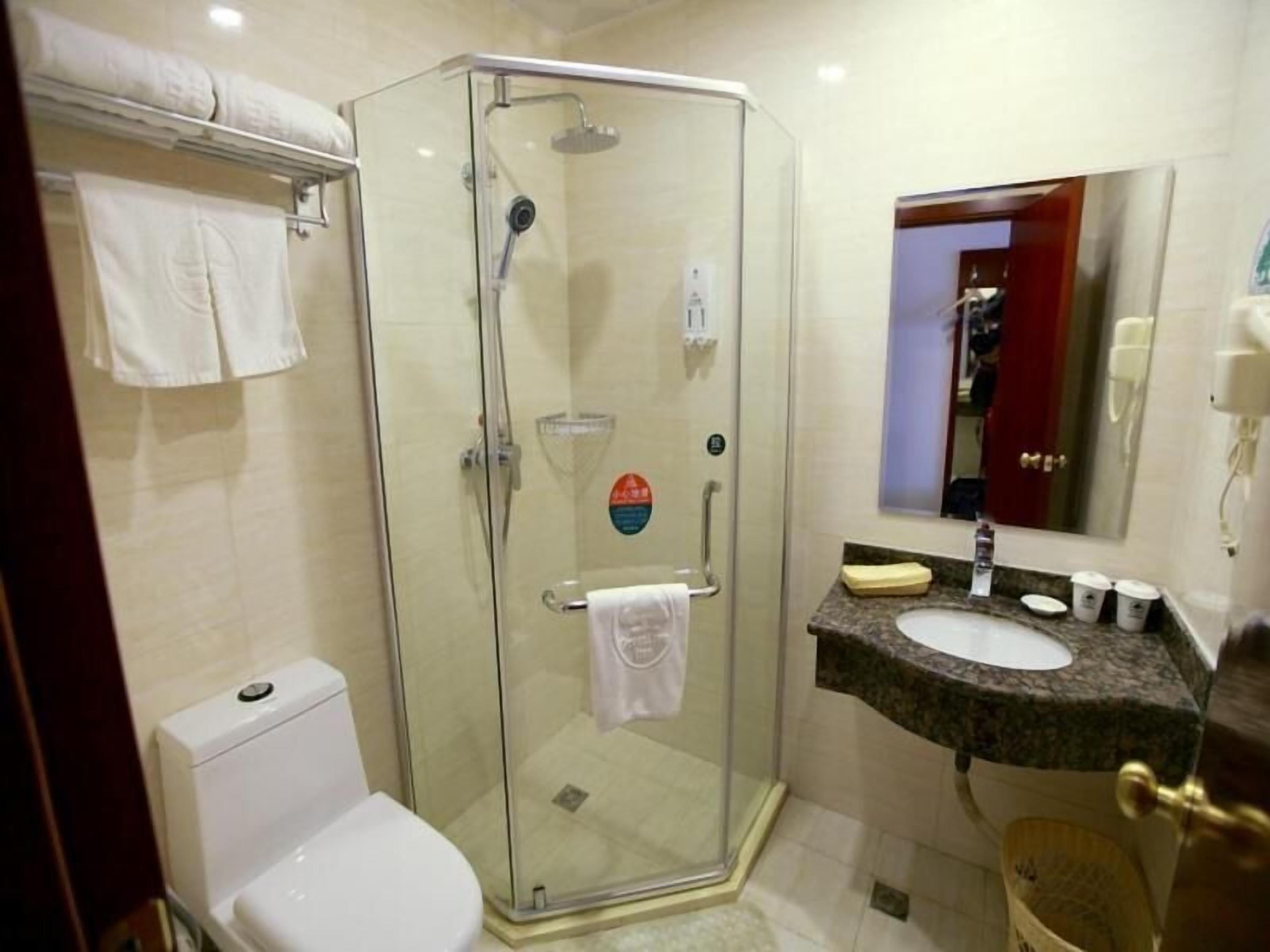 Un baño con ducha envuelta en vidrio, un inodoro blanco, un lavamanos con encimera de granito y un espejo.