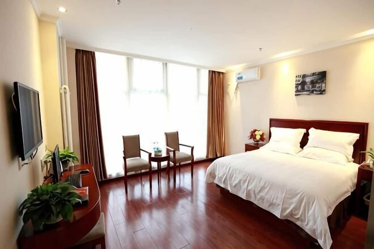 A hotel room with a bed, a desk with a chair, a TV, and a large window with curtains.