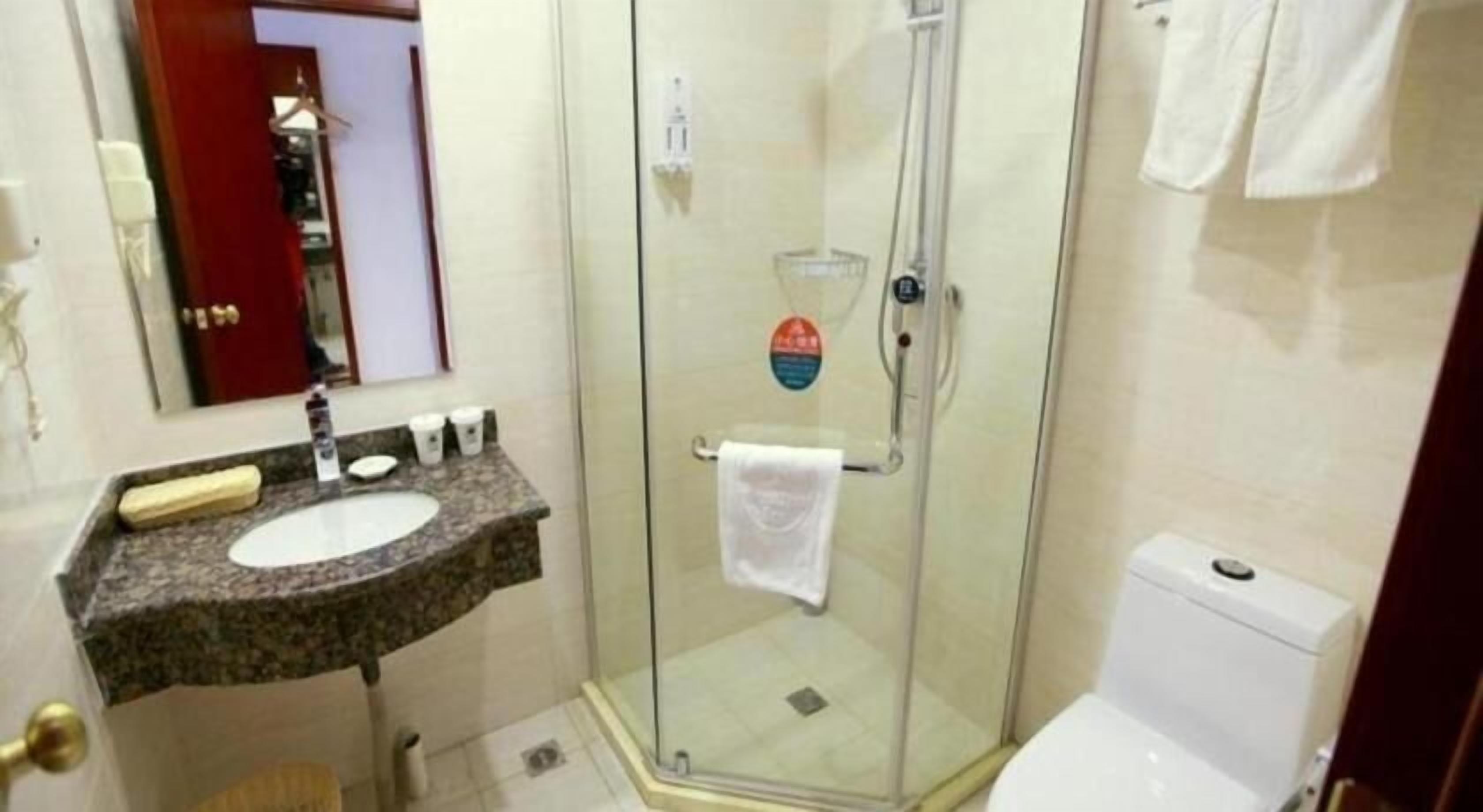 A bathroom with a glass shower enclosure, a sink with a marble countertop, and a toilet.