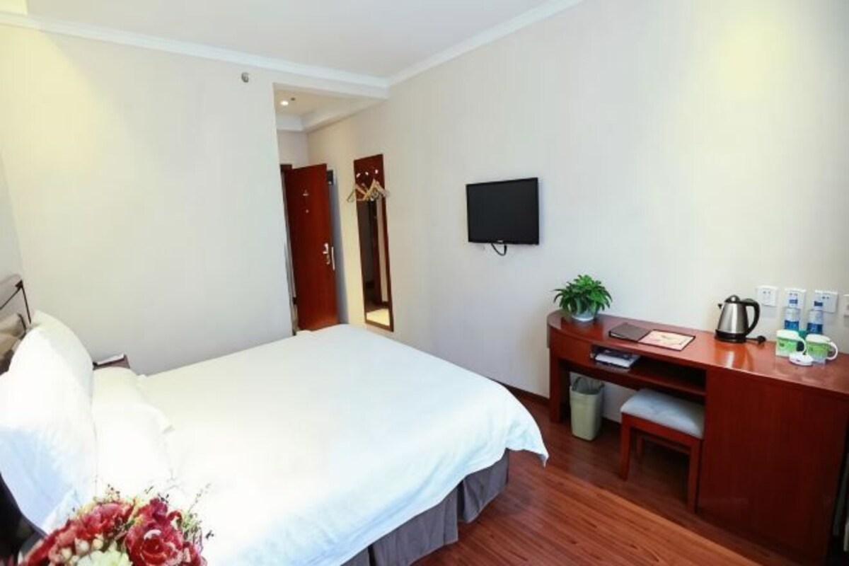 Ein Hotelzimmer mit Bett, Schreibtisch, Stuhl, Fernseher und einer kleinen Pflanze.