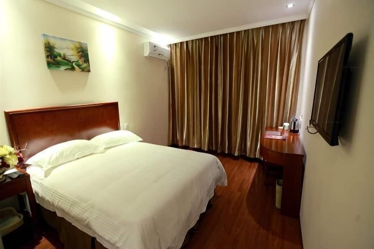 A hotel room with a bed, a desk, a chair, a TV, and a window with curtains.