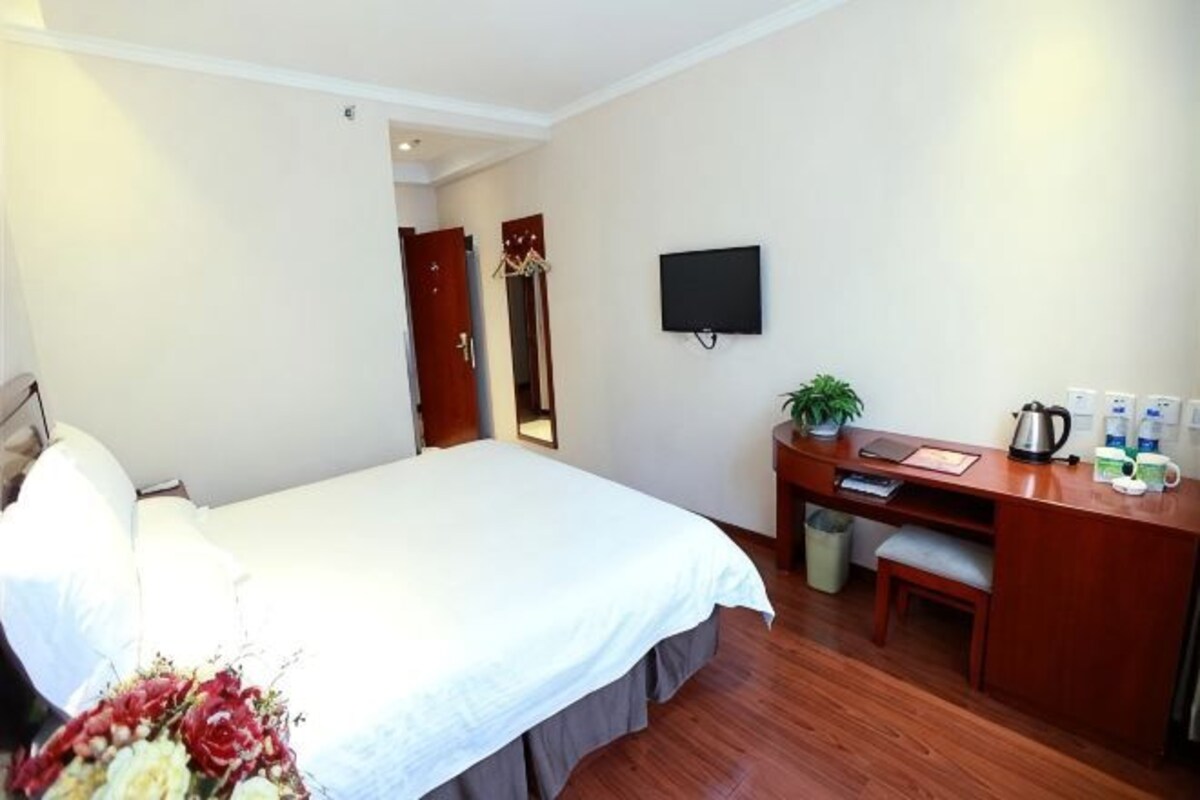 Ein Hotelzimmer mit Bett, Schreibtisch, Stuhl, Fernseher und einer kleinen Pflanze.