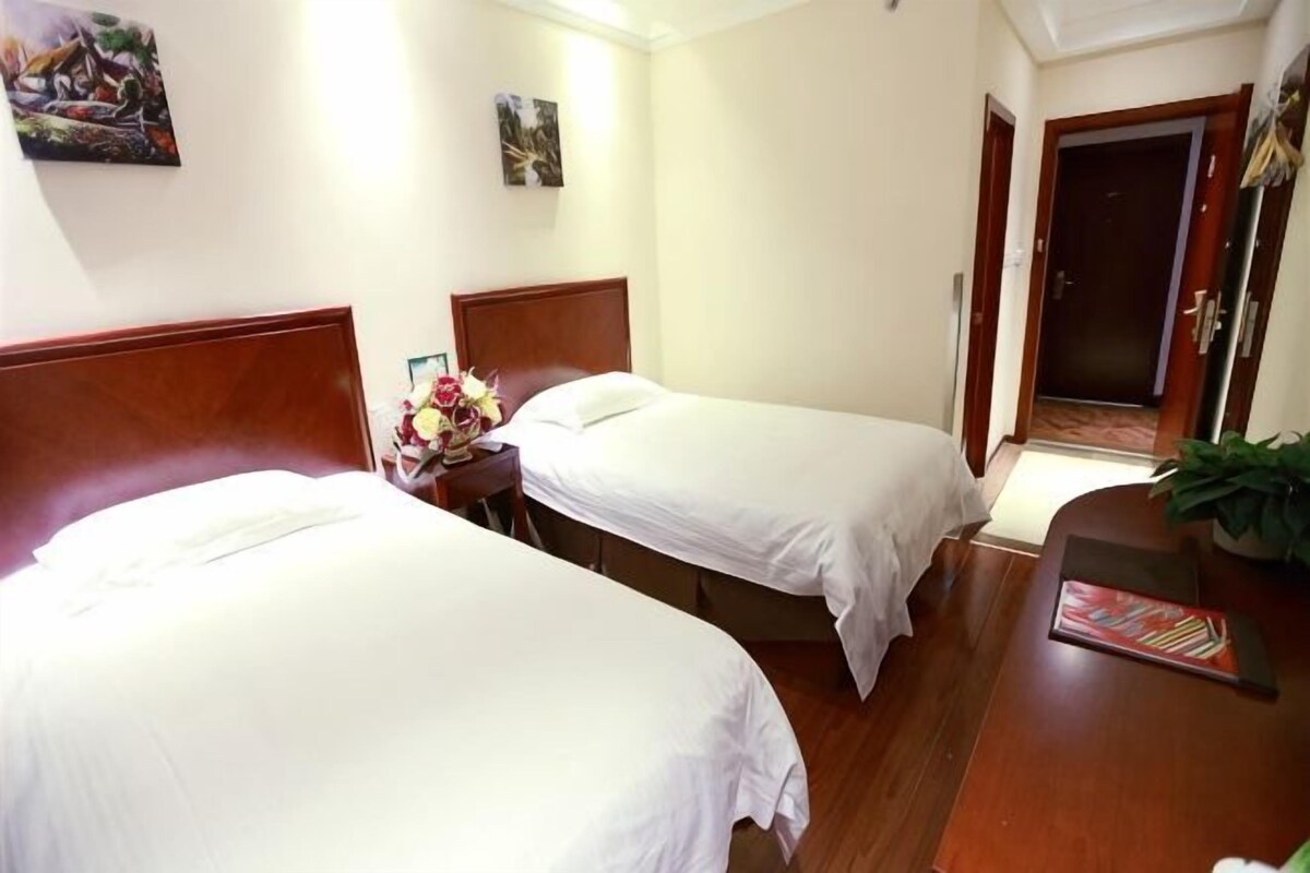 Habitación de hotel con dos camas individuales, cabecera de madera, escritorio con silla y una mesita con un jarrón de flores.