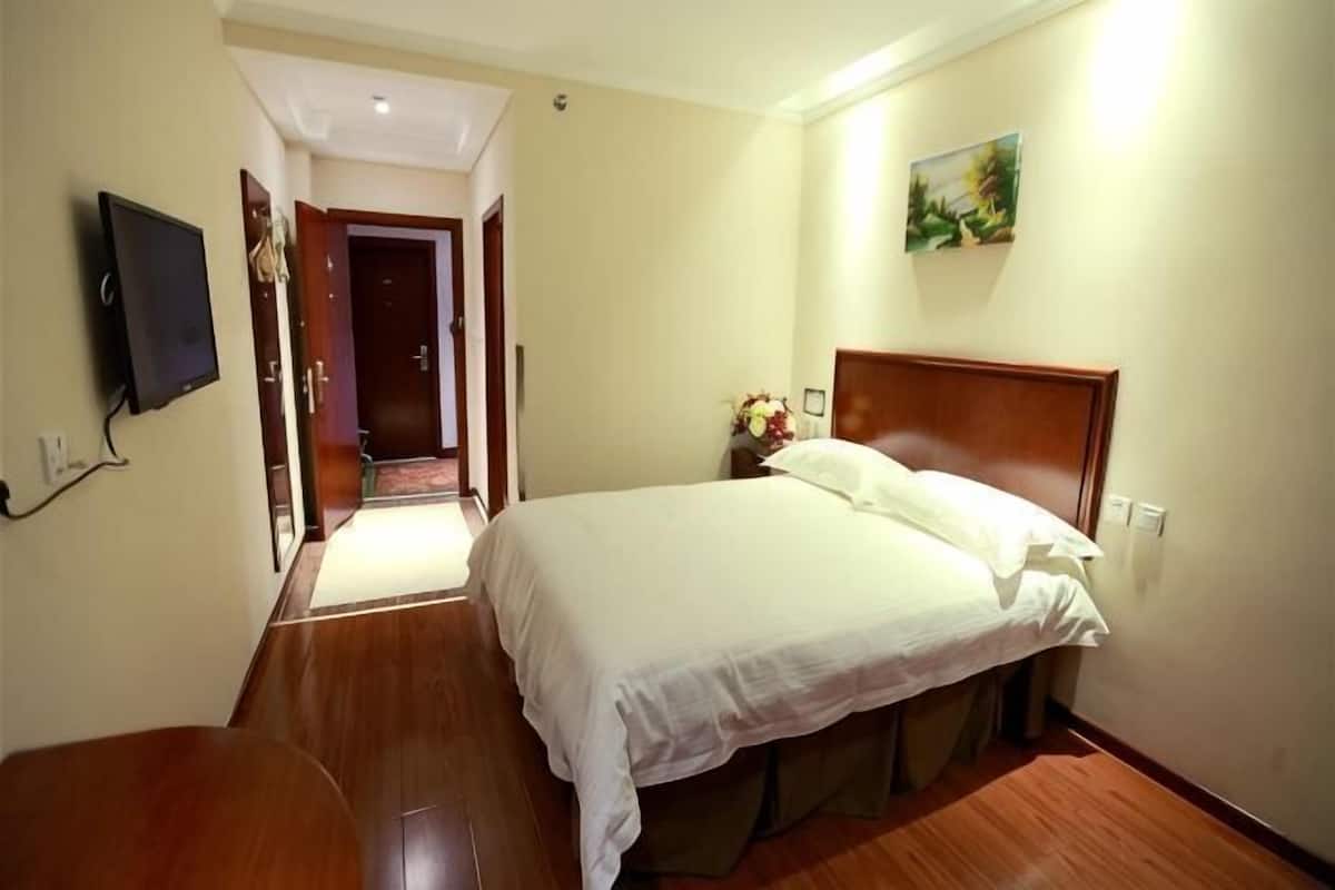 A hotel room with a bed, a TV, a desk, and a painting on the wall.