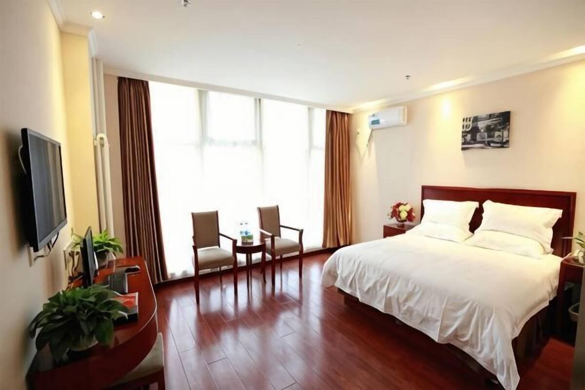 A hotel room with a bed, a desk with a chair, a TV, and a large window with curtains.