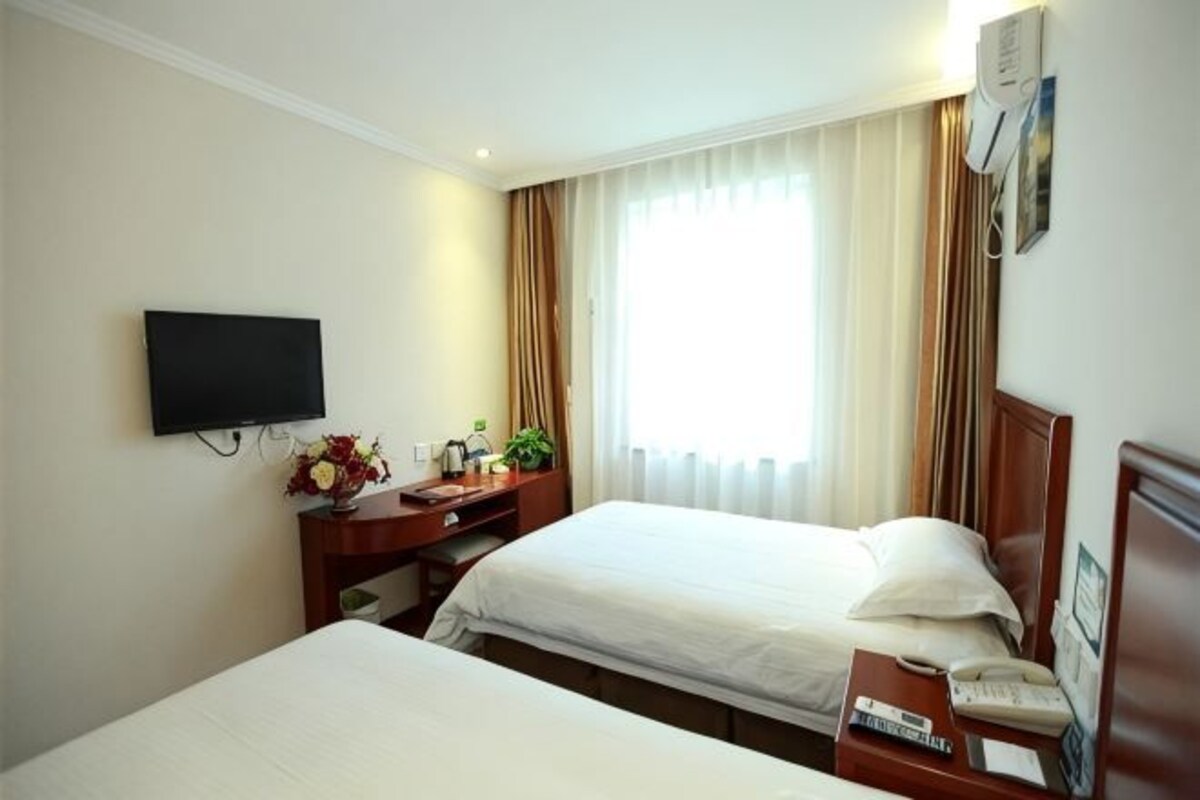 Ein Hotelzimmer mit zwei Betten, einem Fernseher, einem Schreibtisch mit Telefon und einem fenster mit Vorhängen.