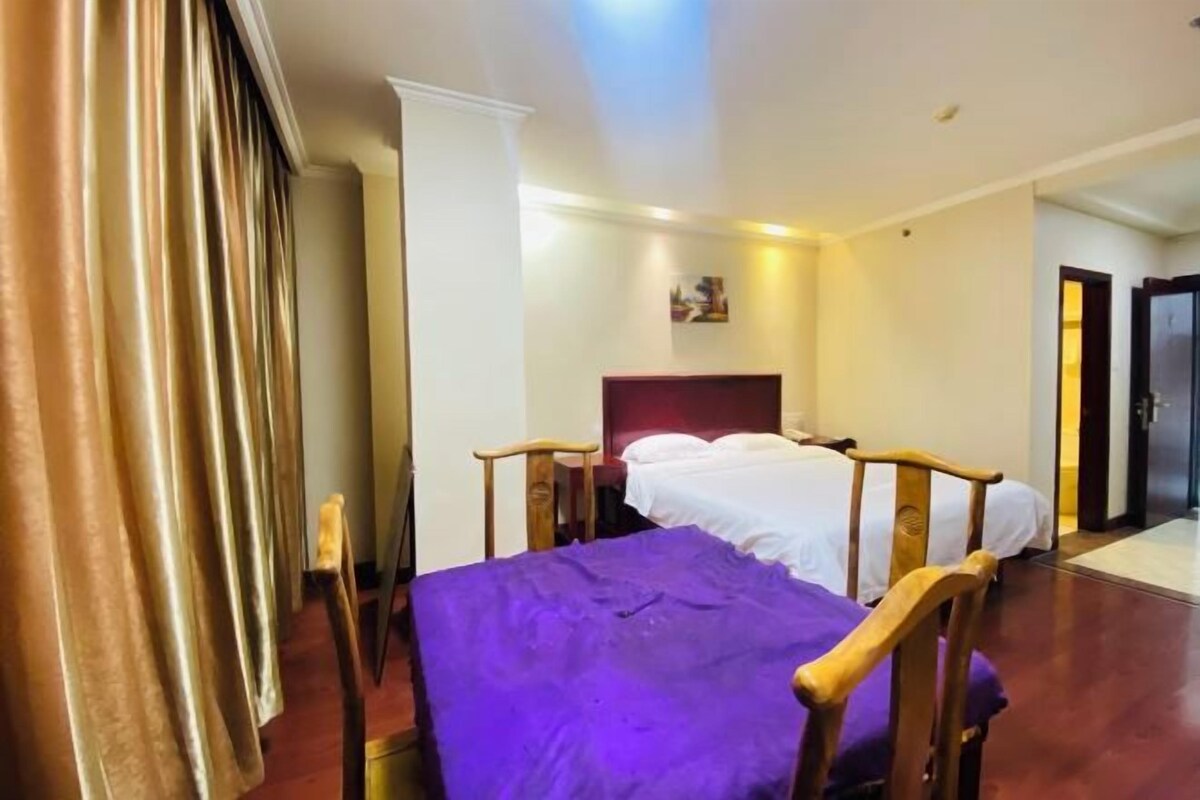 A hotel room with a bed, wooden headboard, and a purple bedspread.