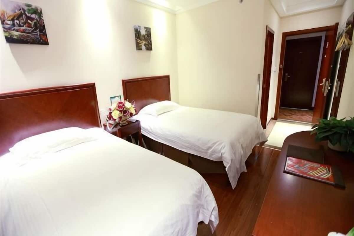 A hotel room with two single beds, a wooden headboard, a desk with a chair, and a small table with a vase of flowers.