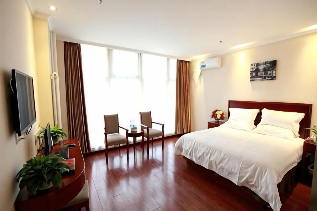 Une chambre d’hôtel avec un lit, un bureau et une chaise, une télévision et une grande fenêtre avec des rideaux.