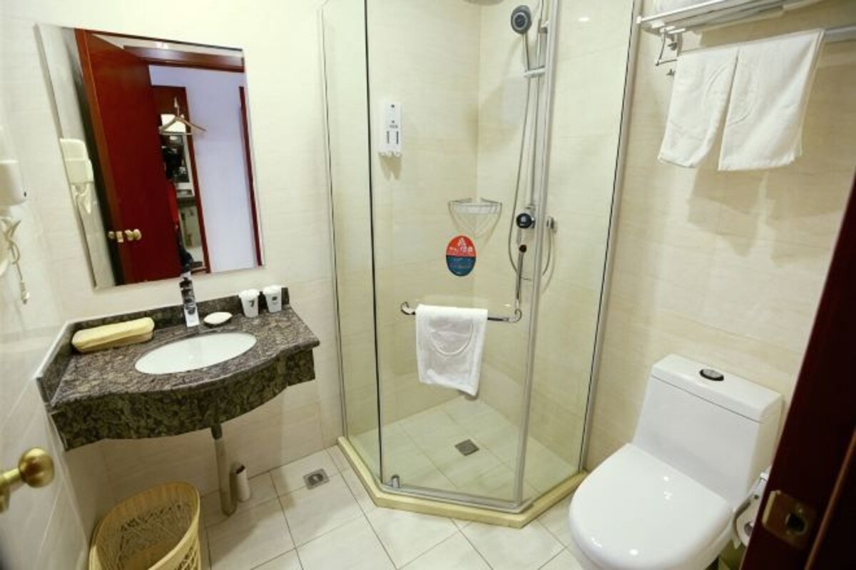 Ein Badezimmer mit Duschkabine aus Glas, einer weißen Toilette, einem Waschbecken mit Marmorplatte und einem Spiegel über dem Waschbecken.