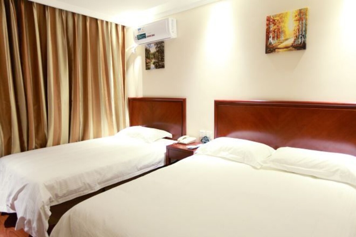 Ein Hotelzimmer mit zwei Einzelbetten, einem Holzkopfende, einer Klimaanlage, einem Nachttisch mit Telefon und einem Bild an der Wand.