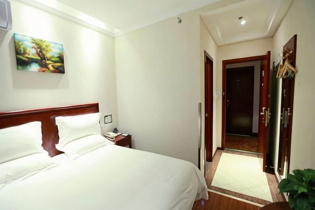 A hotel room with a bed, bedside table, and a painting on the wall.