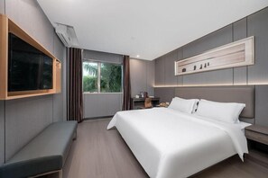 A modern hotel room with a large bed, a bench, a desk, and a window with curtains.