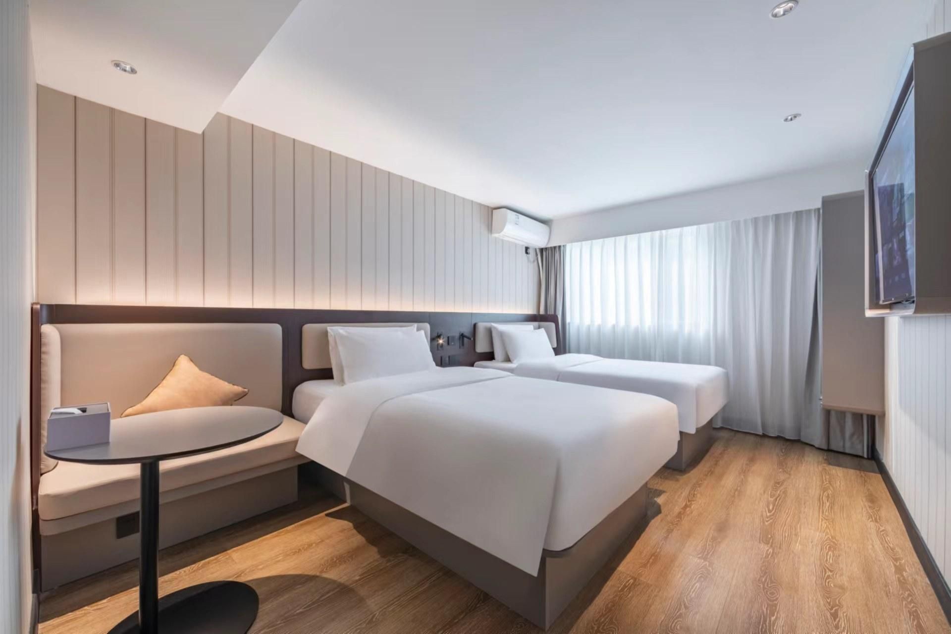 A hotel room with two beds, a sofa, a small table, and a TV.
