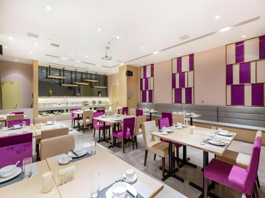A modern dining area with tables and chairs, a kitchen in the background, and a seating area with a sofa.