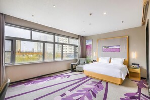 Habitación de hotel con un ventanal grande, una cama, una silla, una mesita de noche y un televisor montado en la pared.