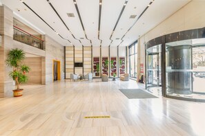 Un vestíbulo amplio con piso de madera pulida, mostrador de recepción, área de estar y ascensor de vidrio.