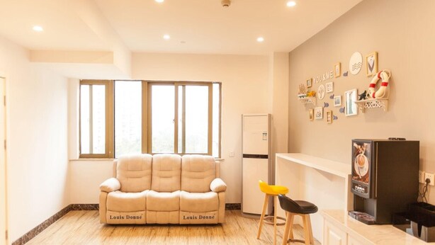 A modern kitchen with a beige sofa labeled "Louis Donné," wooden stools, a refrigerator, and a wall with various framed pictures and a shelf. - Shell Hefei Economic Development Zone Hk Macao Squ (Hefei)