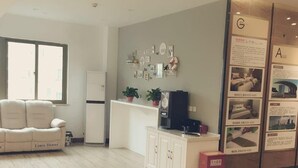 A modern living room with a sofa, a kitchen area with cabinets, a refrigerator, and a wall with framed pictures and a small shelf with plants. - Shell Hefei Economic Development Zone Hk Macao Squ (Hefei)