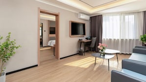 Une chambre d’hôtel moderne avec un plancher en bois, un téléviseur à écran plat fixé au mur, une petite table ornée d’un vase de fleurs et un coin salon avec un canapé et des fauteuils.