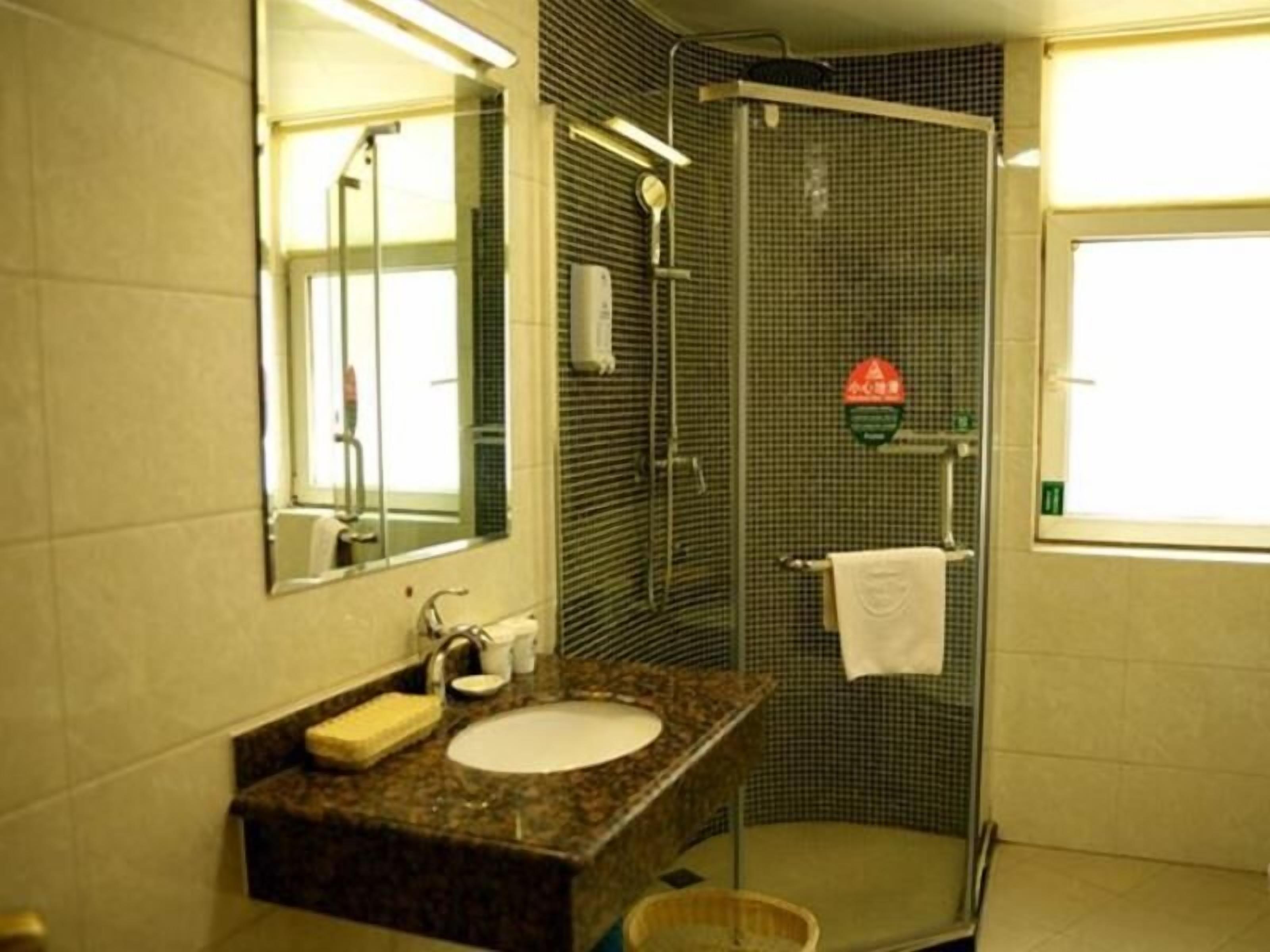 A bathroom with a granite sink, a mirror, a towel rack, and a shower with a safety sign.