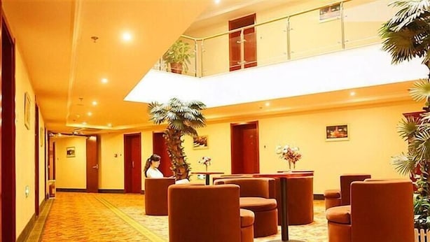 Un hall d’hôtel avec un sol recouvert de moquette, un espace salon avec des fauteuils, un palmier et un escalier.