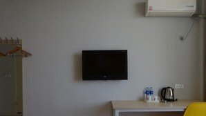 A small room with a white desk, a black TV mounted on the wall, a yellow chair, a water bottle, a kettle, and a trash bin. - Shell Shengyang Huanggu District The Yalv River Yi (Shenyang)