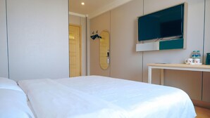 A hotel room with a bed, a TV mounted on the wall, and a desk with a mirror and a few items on it. - Shell Shengyang Huanggu District The Yalv River Yi (Shenyang)