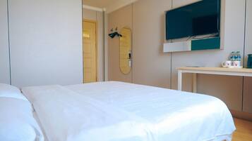 A hotel room with a bed, a TV mounted on the wall, and a desk with a mirror and a few items on it.