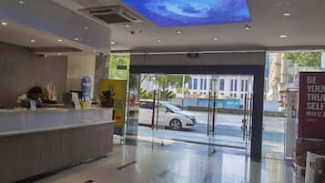 A hotel reception area with a modern design, a reception desk, and a view of the street outside.