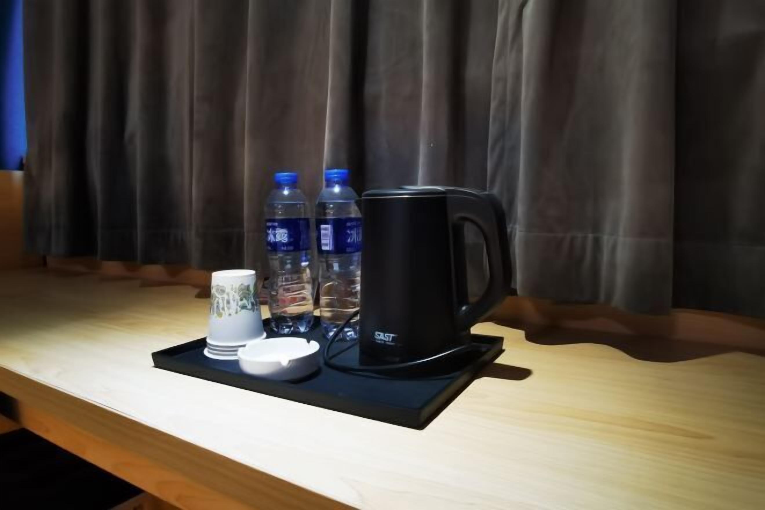 A tray with a black coffee maker, two water bottles, a white mug, and a small white cup on a wooden table.