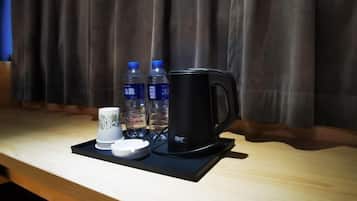 A tray with a black coffee maker, two water bottles, a white mug, and a small white cup on a wooden table.