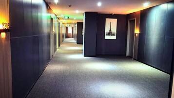 A hotel corridor with a carpeted floor, wall-mounted lights, and a framed picture on the wall.