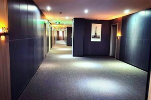 A hotel corridor with a carpeted floor, wall-mounted lights, and a framed picture on the wall. - Baiyi Hotel (Ji'an Municipal Government Branch) (Ji'an)