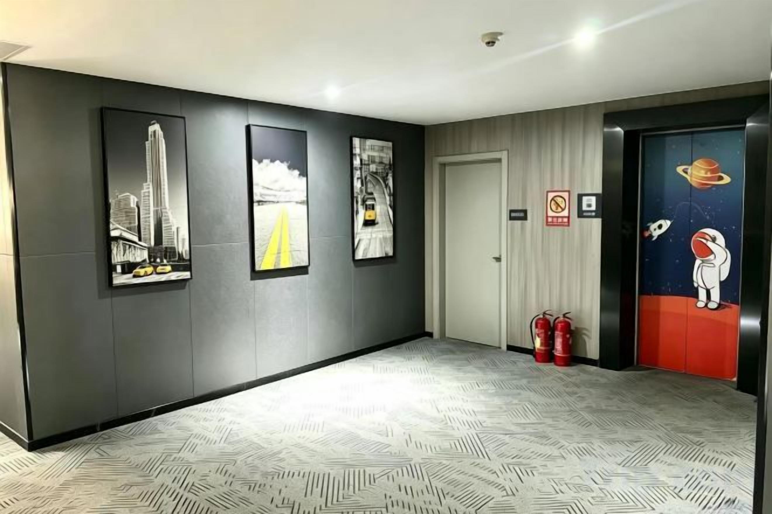 A hallway with framed cityscape and space-themed artwork, a fire extinguisher, and a door with a space-themed mural.
