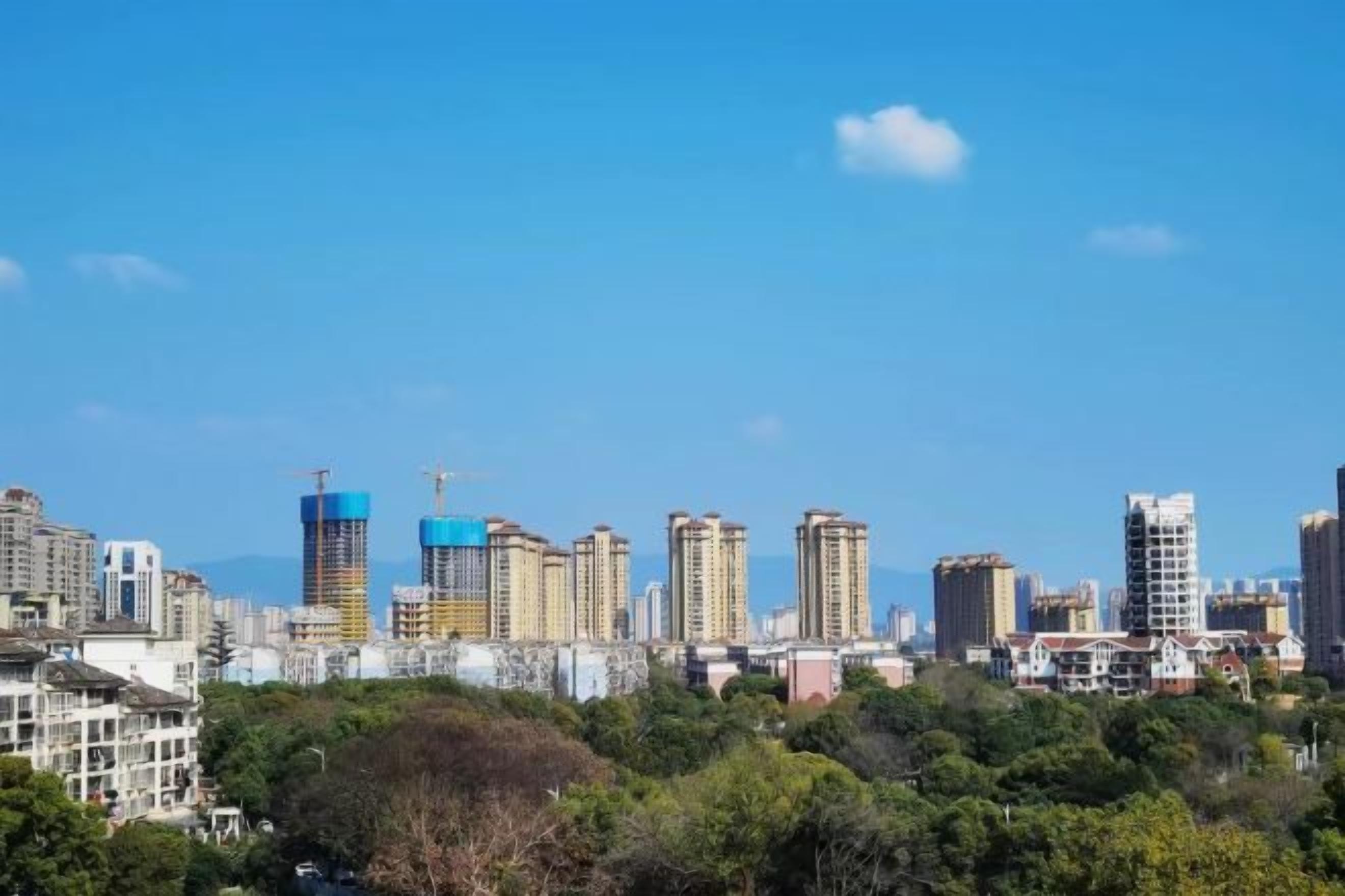 A city skyline with multiple high-rise buildings, some under construction, and a clear blue sky.