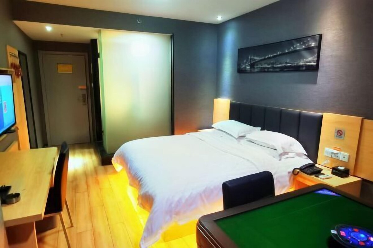 Une chambre d’hôtel avec un lit, un bureau, une télévision, une table de billard et un tableau représentant un paysage urbain accroché au mur.