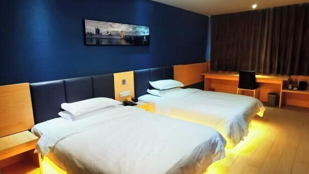 A hotel room with two beds, a dark blue wall, a cityscape painting, and a wooden desk with a chair. - Baiyi Hotel (Ji'an Municipal Government Branch) (Ji'an)