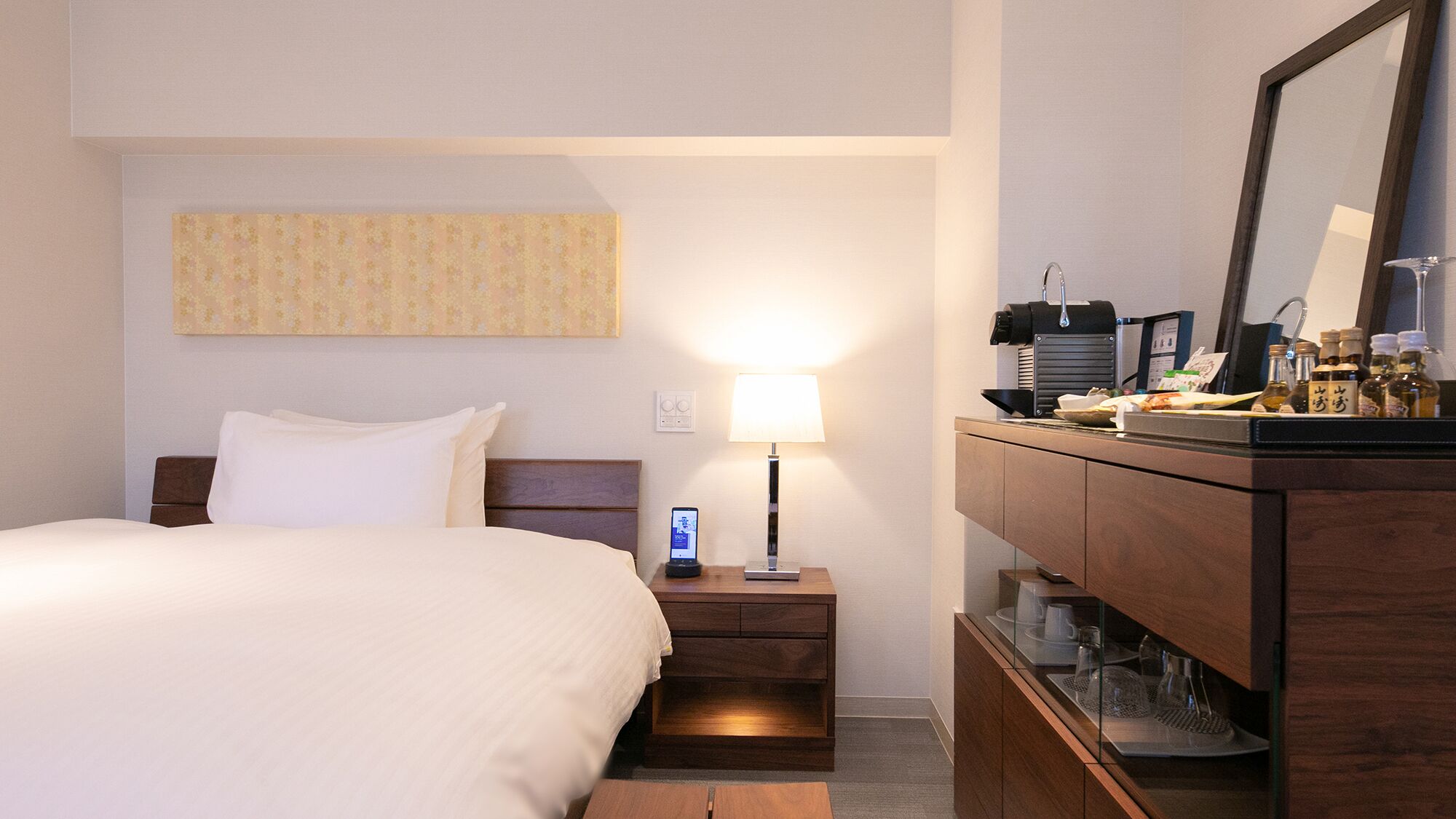 Ein Hotelzimmer mit Bett, Nachttisch, Lampe und einer Minibar.